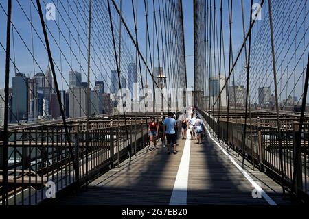 Gehen Sie auf der Brooklyn Bridge mit blauem Himmel über der Skyline von Manhattan in New York City auf eine Spur und fahren Sie mit dem Fahrrad. Stockfoto