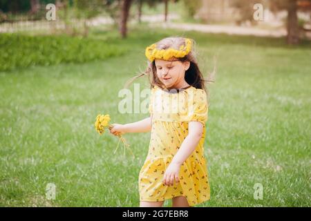 Ein schönes, süßes Mädchen in einem gelben Kleid und mit gelben Delelionen, mit Haaren, die im Wind fliegen, eine Postkarte mit einem hellen sonnigen Tag im Sommer Stockfoto