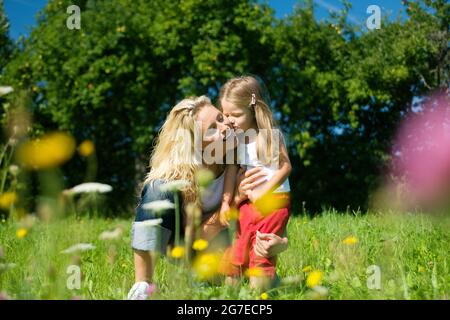 Mutter und Tochter auf einer sonnenbeschienenen Wiese mit vielen Blumen, die sich umarmen Stockfoto