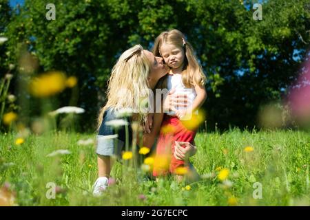 Mutter und Tochter auf einer sonnenbeschienenen Wiese mit vielen Blumen, die sich umarmen Stockfoto