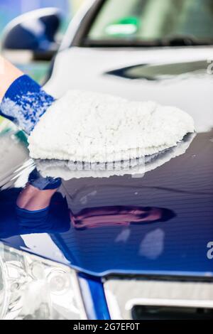 Mann, der die Motorhaube seines blauen Luxuswagens polierte, benutzte einen weichen Handschuh oder einen weichen Handschuh in der Nahaufnahme seiner Hand mit Kopierraum Stockfoto