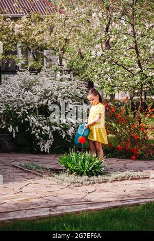 Blühende Bäume und Sträucher im Frühlingsgarten bewässert ein Mädchen an einem sonnigen Frühlingstag Pflanzen aus einer Gartenkannel Stockfoto