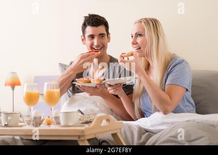 Junges Paar feiern mit Frühstück im Bett sitzen Essen berry Jam o Toast, begleitet von frischen Orangensaft und gekochte Eier. Stockfoto