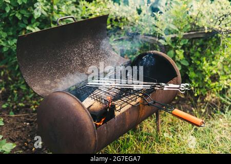 Ein Feuer im Grill zum Grillen machen. Flamme auf dem Hintergrund von grünem Gras am Abend im Hinterhof. Zünden Sie ein Feuer an Stockfoto