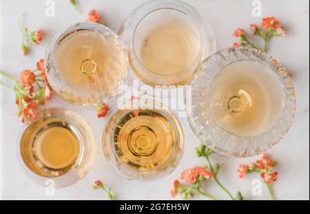 Trendiger Orange- oder Amber-Wein in verschiedenen Gläsern und Blumen auf weißem Hintergrund, Draufsicht, selektiver Fokus. Hautkontakt, Makaration der Haut, wi Stockfoto