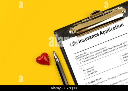 Lebensversicherungsantrag. Zwischenablage mit Zustimmung, Stift und rotem Herz auf einem gelben Schreibtisch. Draufsicht Stockfoto