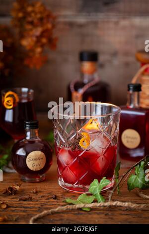 Eine Portion Damson Gin Likör, serviert über Eis mit einer Orangenschale. Flaschen des Likörs umgeben das Glas Stockfoto