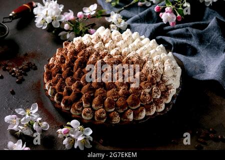 Hausgemachte glutenfreie Tiramisu traditionelle italienische Dessert mit Kakaopulver bestreut verziert mit blühenden Apfelbaum, blaue Textil-Serviette und coff Stockfoto