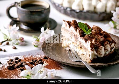 Ein Stück hausgemachtes glutenfreies Tiramisu traditionelles italienisches Dessert, bestreut mit Kakaopulver, verziert mit blühendem Apfelbaum, Kaffee und Minzblättern Stockfoto