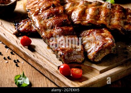 Gegrilltes Schweinefleisch bbq Rippchen serviert mit Kirschtomaten, Basilikum und Barbeque-Sauce auf Holzschneidebrett auf Holzbrett. Nahaufnahme Stockfoto