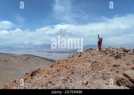 Ein Mann auf dem Gipfel des Vulkans Siete Hermanos, der sich vor einer atemberaubenden Landschaft in der Atacama-Wüste glücklich fühlt Stockfoto