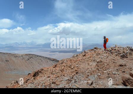 Ein Mann auf dem Gipfel des Vulkans Siete Hermanos blickt in die Ferne zu den trockenen und trockenen Hügeln der Atacama Wüste an der Grenze zu Chile und Argentinien Stockfoto
