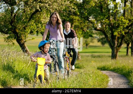 Familie auf einem Ausflug mit ihren Fahrrädern in einer wunderschönen Landschaft, da ihr Sohn so jung ist, dass er ein Trainingsrad fährt Stockfoto