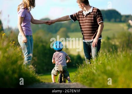 Familie mit jungen Kind einen Wochenendausflug, die Eltern während der Sohn Praktiken ein Training Fahrrad gehen auf Stockfoto