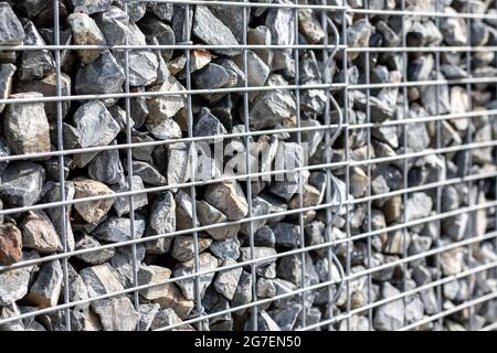 Kleine Granitsteine hinter einem Metallgeflecht, Designzaun, Gartenkonzept Stockfoto