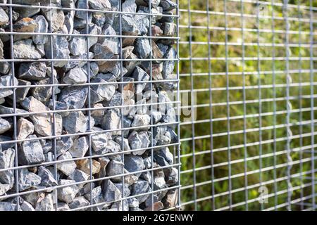 Kleine Granitsteine hinter einem Metallgeflecht, Designzaun, Gartenkonzept Stockfoto