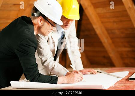 Architekten und Bauingenieure oder Vermessungsingenieure besprechen Pläne und Pläne. Beide tragen Harthüte und stehen auf der Baustelle o Stockfoto
