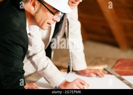 Architekten und Bauingenieure oder Vermessungsingenieure besprechen Pläne und Pläne. Beide tragen Harthüte und stehen auf der Baustelle o Stockfoto