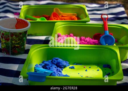 Kinder kinetischer Sand verschiedener Farben in grünen Bädern für die Entwicklung bei Kindern der nützlichen Fähigkeiten. Stockfoto