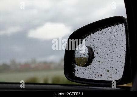 Regentropfen auf einem Autospiegel vor dem Hintergrund von Regenwolken. Stockfoto