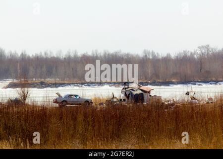 Das Winterhaus eines heruntergekommenen Flüchtlings aus Industriemüll und sein altes rostiges Auto. Stockfoto