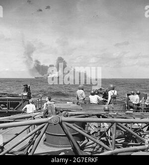 USS Intrepid (CV-11), nachdem sie von einem japanischen Flugzeug bei einem Selbstmordtauchgang im Pazifik getroffen wurde. Aufgenommen von der USS New Jersey (BB-62). Rauch von USS Intrepid (CV-11) Kanonierern bei 40mm Kanonen an Bord der USS New Jersey (BB-62) im Vordergrund Stockfoto
