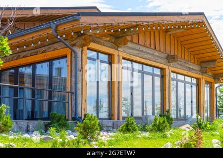 Schönes Holzhaus mit großen Buntglasfenstern auf dem Hintergrund des Sommerhimmels Stockfoto