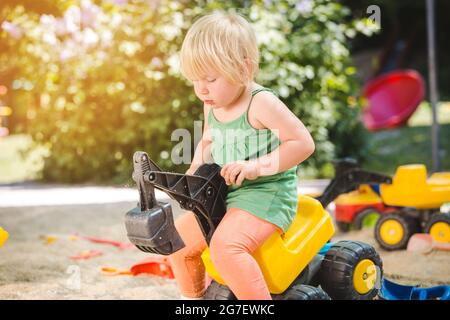 Mädchen Kind Reiten auf einem gelben Spielzeug Traktor auf dem Spielplatz Stockfoto