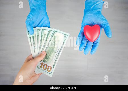 Ärztin Hände in blauen Handschuhen nahmen Geld statt Herz. Korruption im Gesundheitswesen. Bezahlte Medikamente. Kosten für die Krankenversicherung. Stockfoto