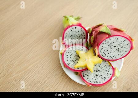 Scheiben Drachenfrucht oder Pitaya mit weißem Fruchtfleisch und schwarzen Samen auf weißem Teller mit einer Scheibe Starfrucht oder averrhoa carambola. Exotische Früchte Stockfoto