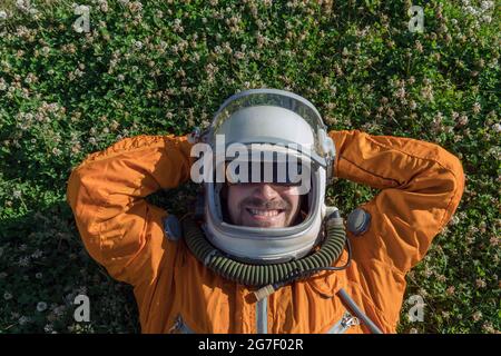 Glücklicher Kosmonaut, der Helm mit Sonnenbrille und Raumanzug trägt und sich draußen ausruhen kann Stockfoto