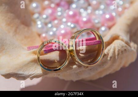 Ein Paar goldene Ehering-Bänder Schmuck auf Muschel mit rosa und weißen Perlenperlen Stockfoto