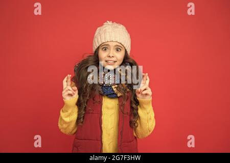 Überrascht hübsches Mädchen in Kugelweste mit Strickmütze und Pullover Daumen drücken, einen Wunsch machen Stockfoto