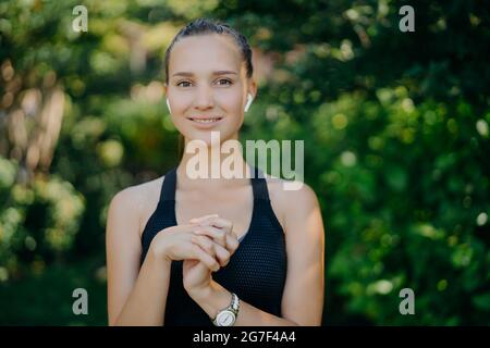 Die Außenaufnahme einer ziemlich dunkelhaarigen Frau hält die Hände zusammen, da sie in guter körperlicher Verfassung ist, da sie regelmäßig Sportleinen trägt Stockfoto