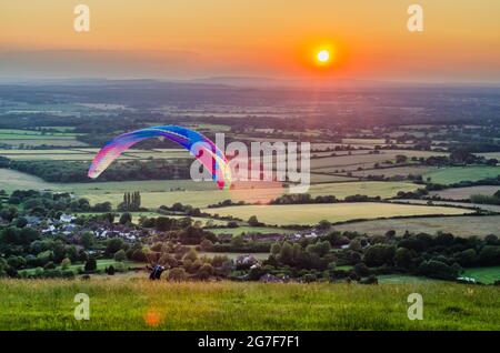 Devils Dyke, Brighton, East Sussex, Großbritannien. Juli 2021. Wind aus nördlicher Richtung bringt Gleitschirmflieger zu den herrlichen South Downs nördlich von Brighton. Der Gleitschirm startet in die untergehende Sonne über die neblige Landschaft. Kredit: David Burr/Alamy Live Nachrichten Stockfoto