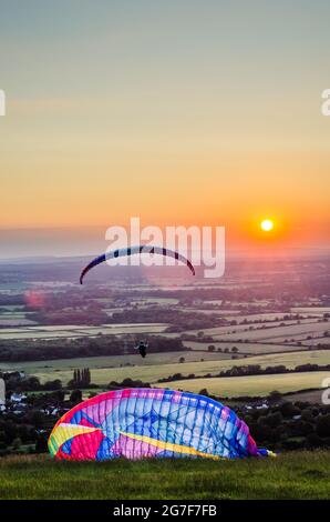 Devils Dyke, Brighton, East Sussex, Großbritannien. Juli 2021. Wind aus nördlicher Richtung bringt Gleitschirmflieger zu den herrlichen South Downs nördlich von Brighton. Gleitschirme starten in die untergehende Sonne über die neblige Landschaft. Kredit: David Burr/Alamy Live Nachrichten Stockfoto