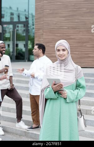 Porträt einer modernen jungen islamischen Frau in Hijab- und Nationaltracht, die mit Tablet im Freien steht Stockfoto