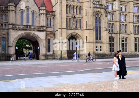 Ein männlicher Absolvent in Abschlusskostüm und ein Freund stehen vor der Whitworth Hall an der University of Manchester, Manchester, Großbritannien Stockfoto