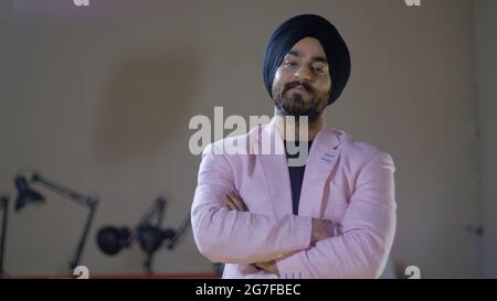 Junger indischer Geschäftsmann, der einen Sikh-Turban trägt und mit gekreuzten Händen posiert Stockfoto