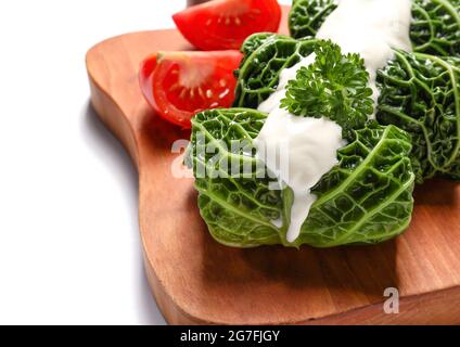 Brett mit gefüllten Kohlblättern, Sauerrahm und geschnittenen Tomaten auf weißem Hintergrund, Nahaufnahme Stockfoto