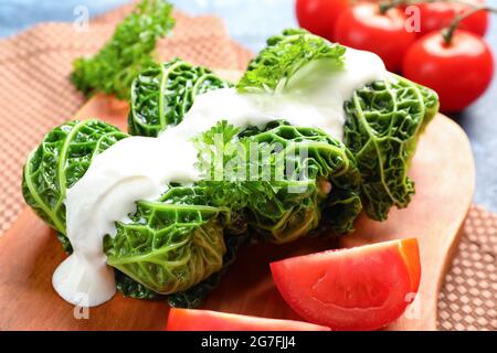 Brett mit gefüllten Kohlblättern, saurer Creme und Tomaten auf farbigem Hintergrund, Nahaufnahme Stockfoto