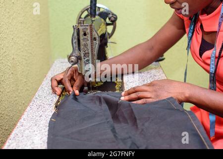Eine fleißige afrikanische Schneiderin, Modedesignerin oder Kleidermacherin, die mit einer Nähmaschine stilvolle und modische Kleidung in einer Schneiderei macht Stockfoto
