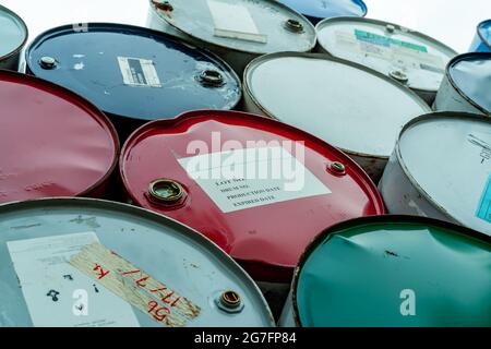 Alte Chemiefässer stapeln sich. Rote, grüne und blaue chemische Trommel. Stahltank mit brennbaren Flüssigkeiten. Gefährliche Chemikalienfass. Industrieabfälle. Stockfoto