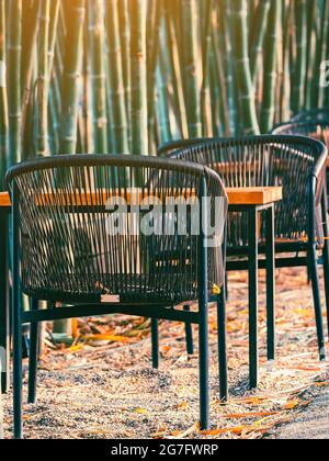 Stühle und Tische zum Sitzen und Entspannen am Weg im natürlichen grünen Bambusgarten. Entspannungsatmosphäre im Freien mit Gartengestaltung im Restaurant Stockfoto