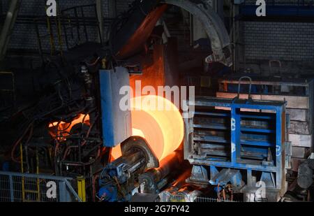 13. Juli 2021, Brandenburg, Eisenhüttenstadt: Im Warmwalzwerk von ArcelorMittal wird eine rotheiße Platte in eine Spule gewickelt. Die verwendeten Platten sind 225 Millimeter dick und bis zu 12 Meter lang. Aus den Brammen werden Heißband-Coils mit einem maximalen Gewicht von 34 t hergestellt. Foto: Soeren Sache/dpa-Zentralbild/dpa Stockfoto