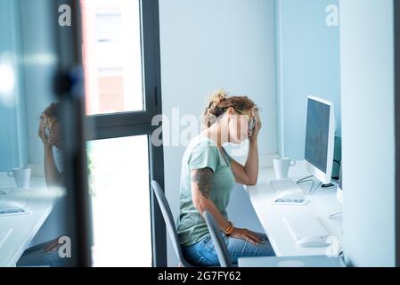 Gestresste und müde Erwachsene junge Frau am Desktop vor dem Computer und Online-Job Aktivität Tag Lebensstil berühren ihren Kopf für Kopfschmerzen Schmerzen - o Stockfoto