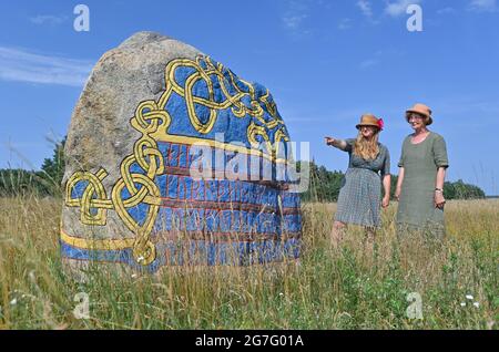 13. Juli 2021, Brandenburg, Henzendorf: Dorothee Schmidt-Breitung (l.), Restauratorin, und Ilona Weser vom Landschaftsschutzverband stehen vor einem in Stein gemeißelten Schild und Figuren auf einem erratischen Felsbrocken auf dem Gelände des erratischen Felsbrockparks Henzendorf. Diese Zeichnungen wurden im vergangenen Jahr restauriert. Der erratische Blockpark mit seinen rund 100 behauenen und bemalten erratischen Blöcken entstand 1997. Moos und Flechten wachsen seit über 20 Jahren auf den Steinen und die Farben verblassen allmählich. Im Jahr 2020 wurden 18 Steine restauriert. Derzeit unter der Leitung von Restauratoren D Stockfoto