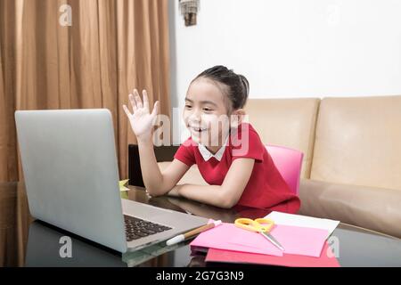 Asiatische kleine Mädchen mit Laptop Teilnahme an Online-Schulklasse zu Hause. Online-Bildung während der Quarantäne Stockfoto