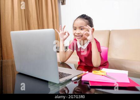 Asiatische kleine Mädchen mit Laptop Teilnahme an Online-Schulklasse zu Hause. Online-Bildung während der Quarantäne Stockfoto