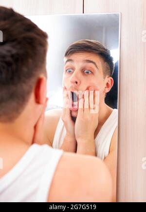 Überrascht junger Mann Blick auf Reflexion in der Spiegel in Das Zimmer Stockfoto